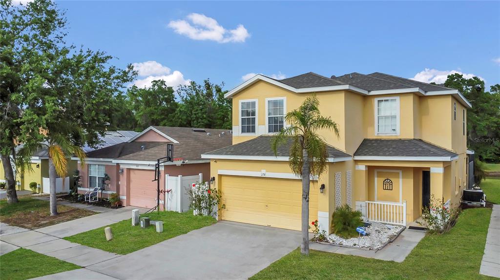 A two-story yellow house with a two-car garage and a palm tree in the front — 178 HAMMOCK COURT, DAVENPORT, FL