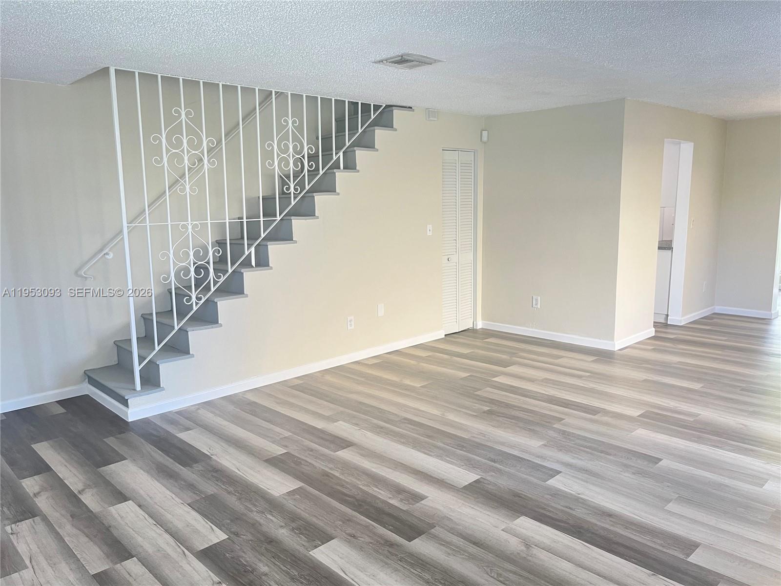 An empty room features gray wood-look flooring, beige walls, and a white decorative metal staircase railing — 9503 SW 88th Ter # 9503, Miami FL 33176, MIAMI, FL