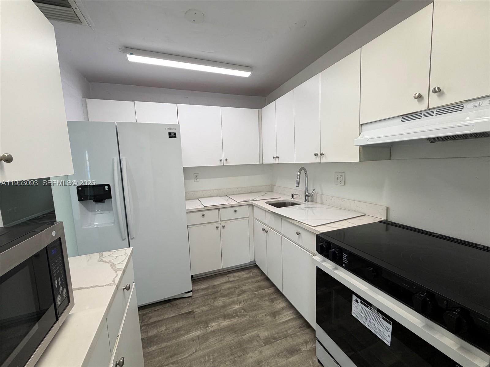 A kitchen features white cabinets, a white refrigerator, a black stove, and wood-look flooring — 9503 SW 88th Ter # 9503, Miami FL 33176, MIAMI, FL
