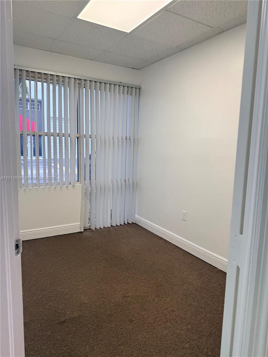 An empty office features brown carpeting, white walls, and vertical blinds covering a window — 12311 SW 133rd Ct # 23, Miami FL 33186, MIAMI, FL