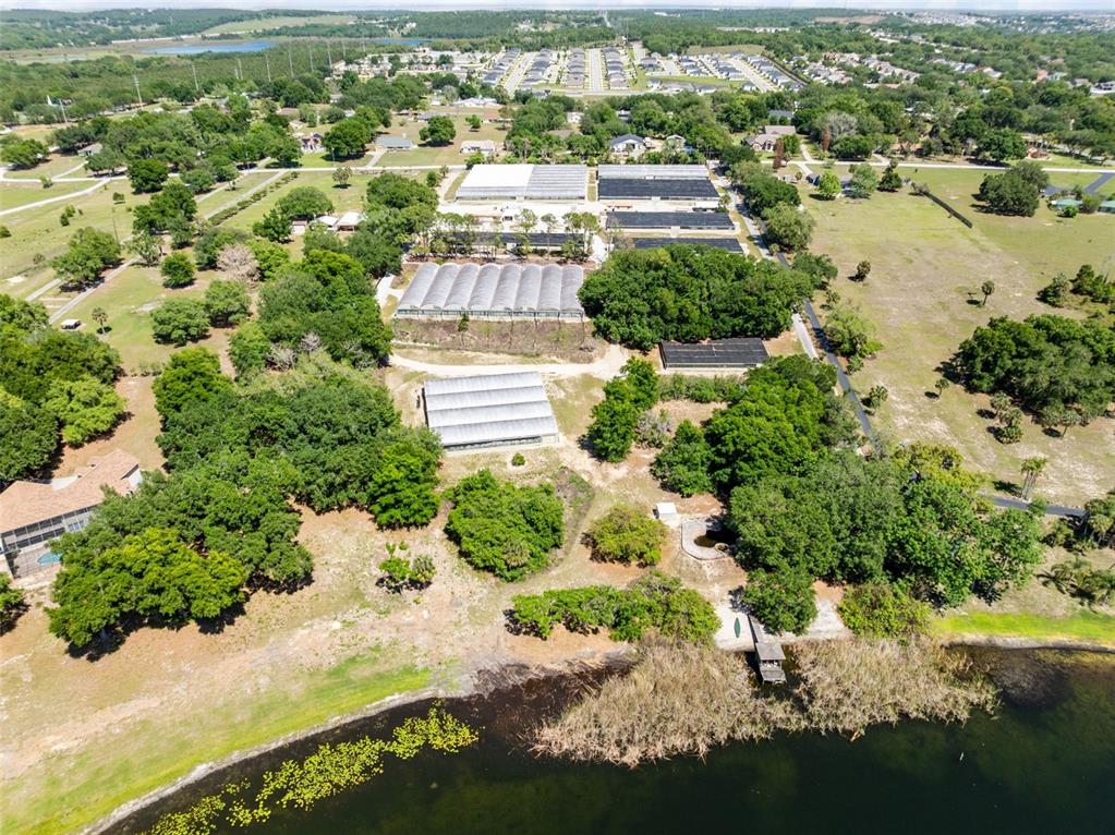 An aerial view shows a property with several greenhouses, mature trees, and a private dock — 18021 E APSHAWA ROAD, MINNEOLA, FL