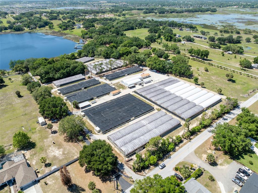An aerial view shows a commercial greenhouse facility with multiple structures near a lake — 18021 E APSHAWA ROAD, MINNEOLA, FL