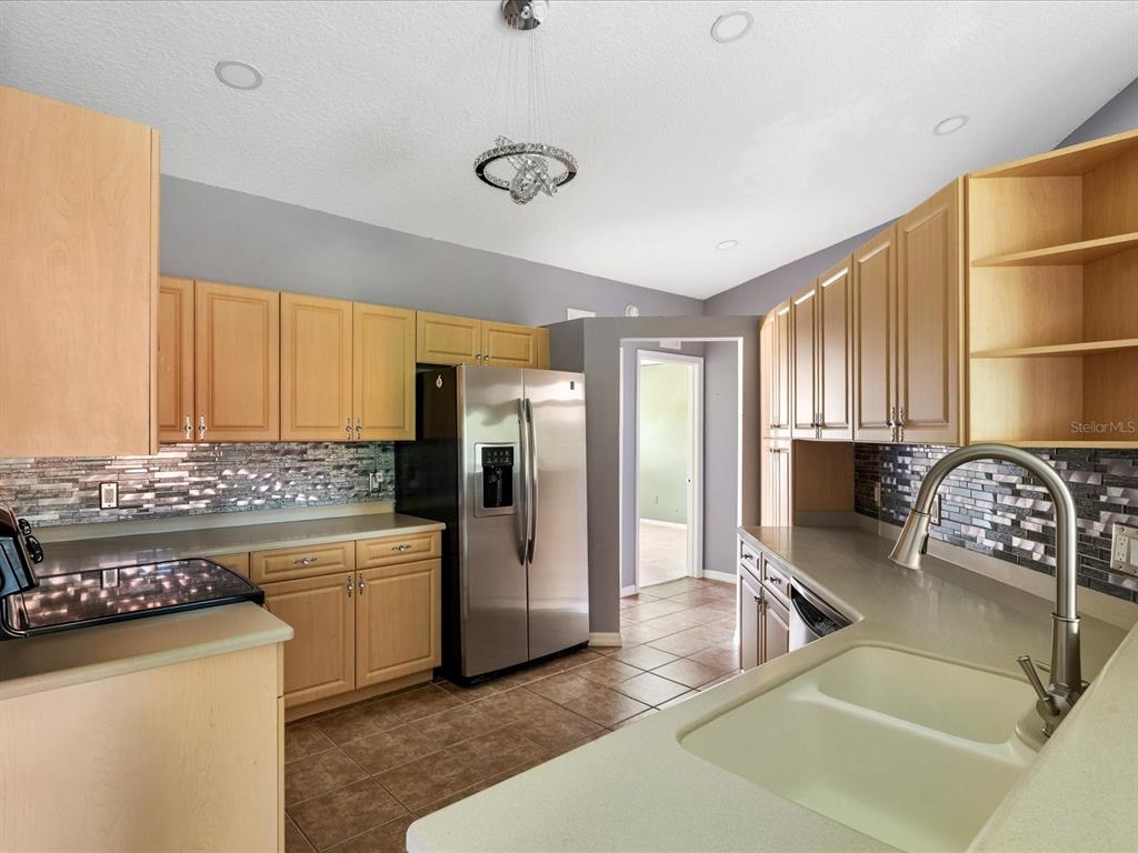 A kitchen features light wood cabinets, stainless steel appliances, a tiled backsplash, and tile flooring — 5336 EDGEWATER WAY UNIT 11, OXFORD, FL