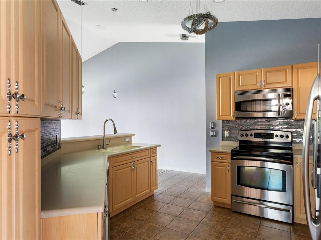 A kitchen with light wood cabinets, stainless steel appliances, tile flooring, and a breakfast bar — 5336 EDGEWATER WAY UNIT 11, OXFORD, FL