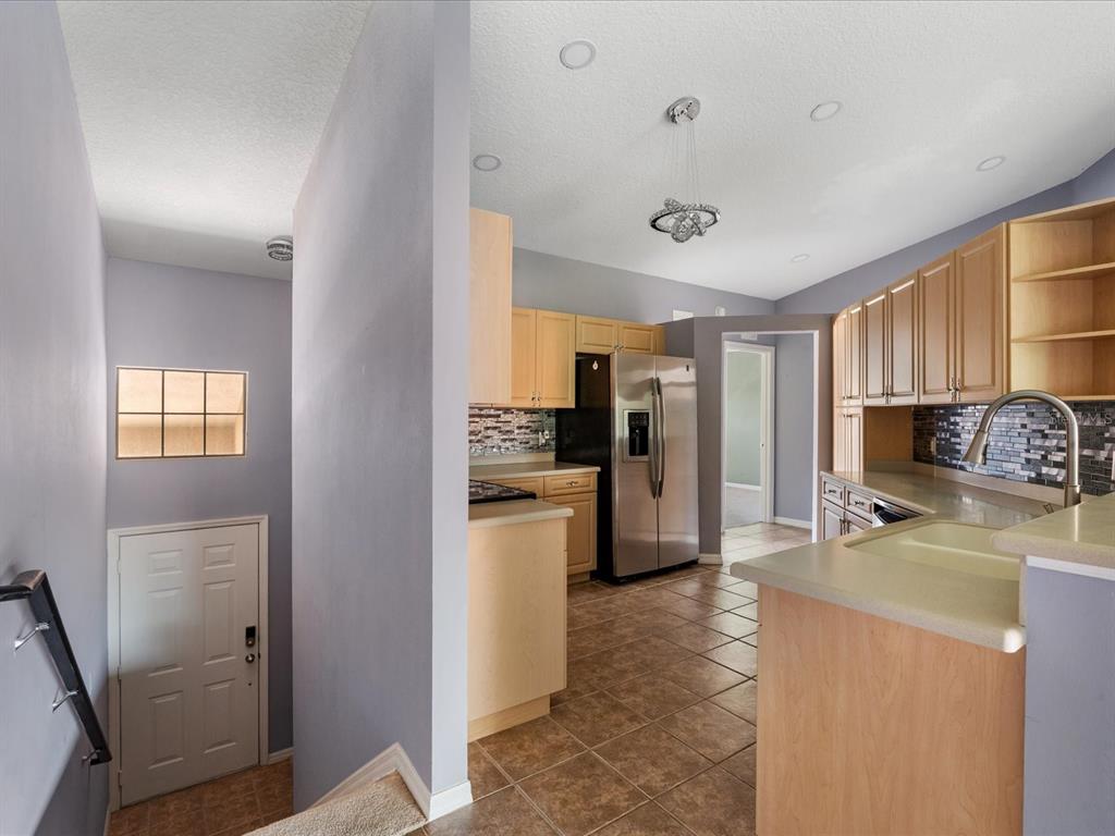 A kitchen with light wood cabinets, stainless steel appliances, and tile flooring overlooks a staircase — 5336 EDGEWATER WAY UNIT 11, OXFORD, FL