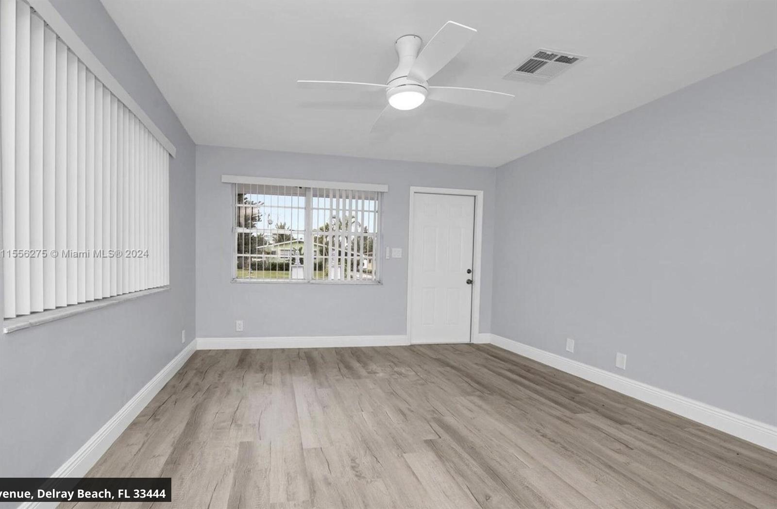 An empty room features light gray walls, wood-look flooring, a ceiling fan, and two windows — 145 SW 13th Avenue, Delray Beach FL 33444, DELRAY BEACH, FL