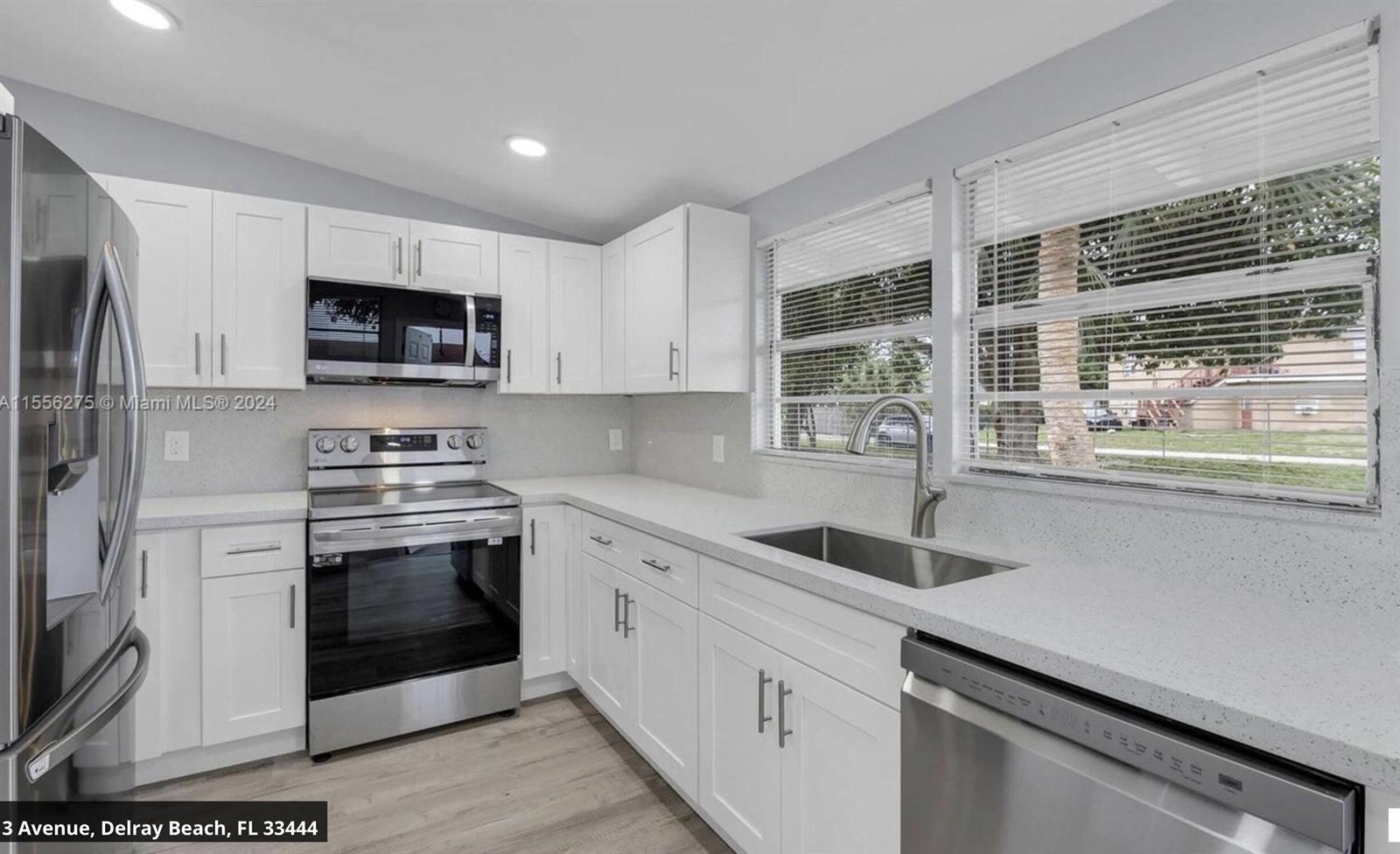 A kitchen features white cabinets, stainless steel appliances, and light countertops under a window — 145 SW 13th Avenue, Delray Beach FL 33444, DELRAY BEACH, FL