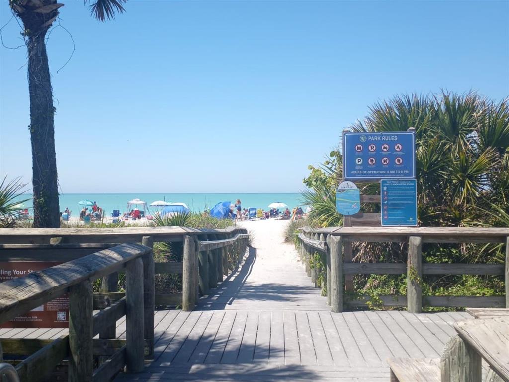 A wooden boardwalk leads to a sandy beach with people and umbrellas under a clear sky — 124 WAHOO DRIVE, ROTONDA WEST, FL