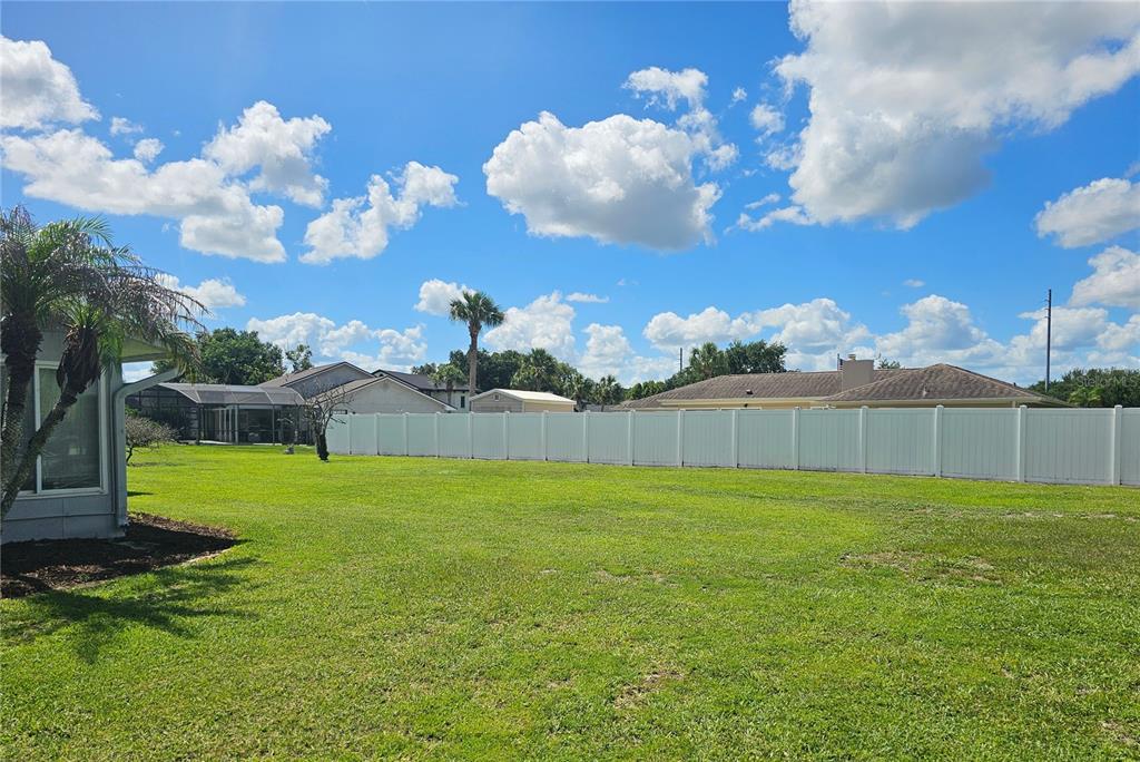 A large, grassy backyard features a white vinyl privacy fence and a nearby residential home — 1850 CHAUCER WAY, KISSIMMEE, FL