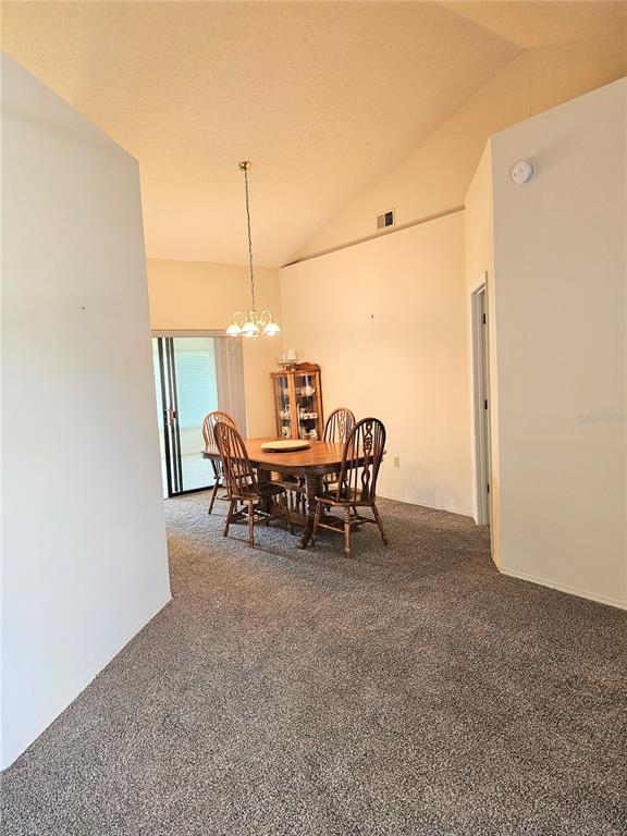 A dining room with carpeted floors, a wooden table with chairs, and a vaulted ceiling — 1850 CHAUCER WAY, KISSIMMEE, FL
