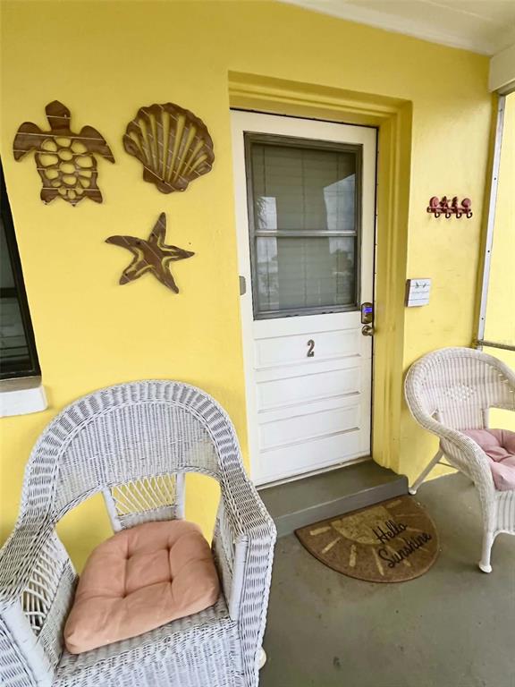 A yellow exterior porch features two white wicker chairs, a door numbered two, and wall decor — 6802 GULF WINDS DRIVE, ST PETE BEACH, FL