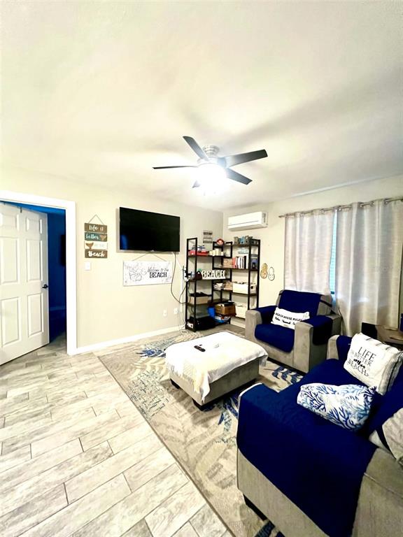 A living room features a ceiling fan, a wall-mounted television, a storage ottoman, and furniture — 6802 GULF WINDS DRIVE, ST PETE BEACH, FL