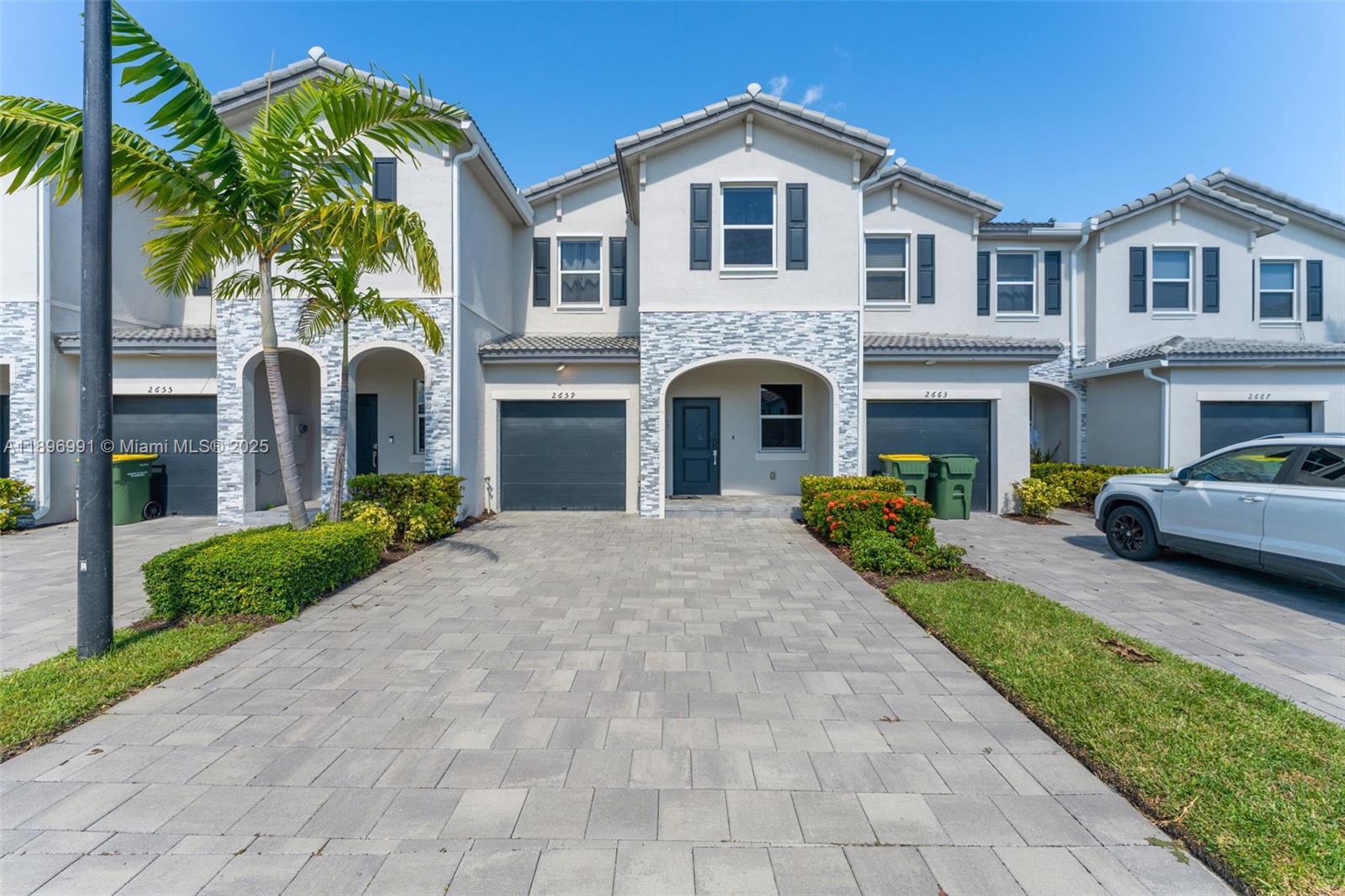A row of two-story townhouses features paved driveways, stone accents, and attached garages — 2659 SE 11th St, Homestead FL 33035, HOMESTEAD, FL