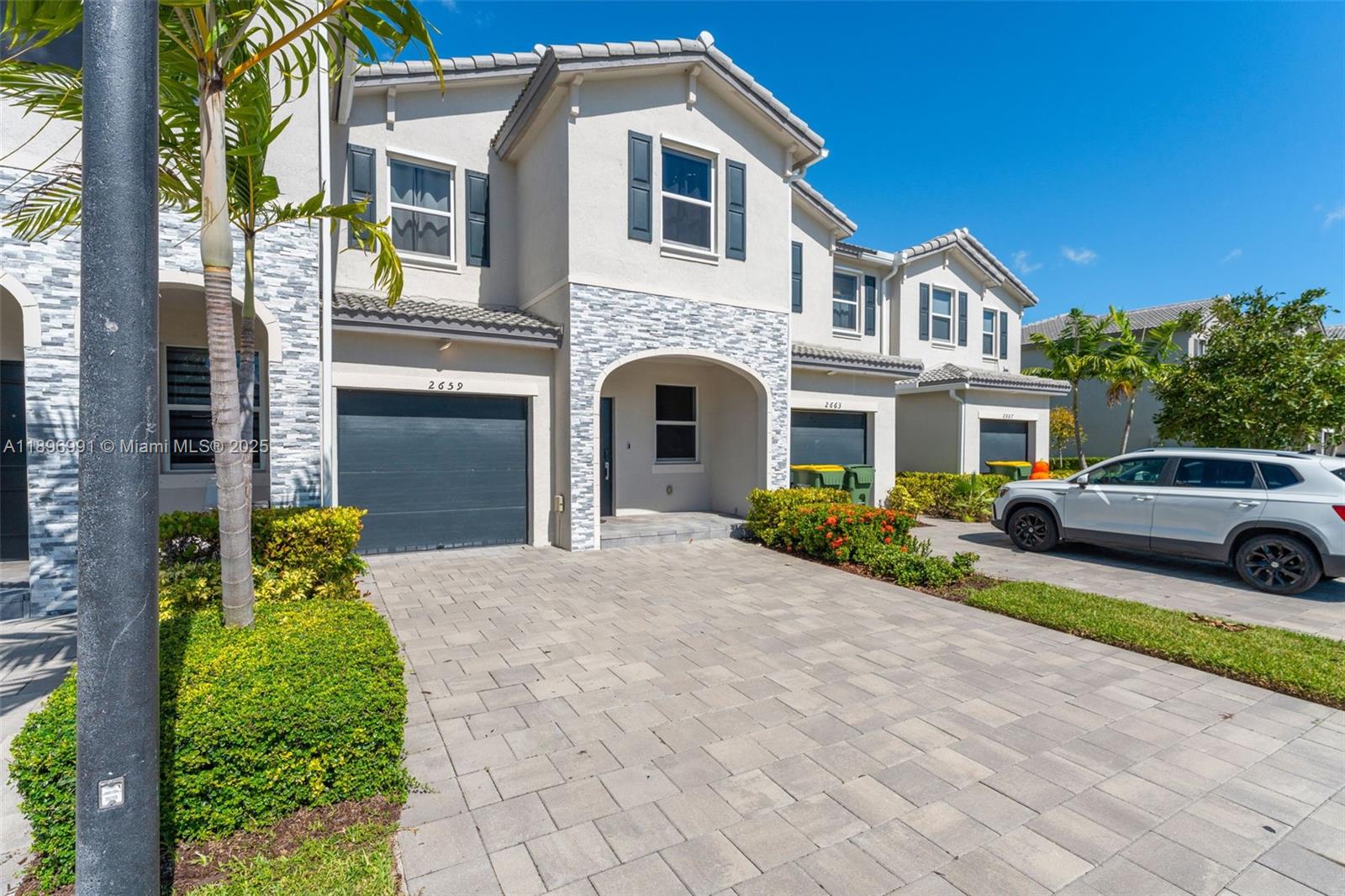 A row of two-story townhouses features stone-accented facades, paved driveways, and dark garage doors — 2659 SE 11th St, Homestead FL 33035, HOMESTEAD, FL