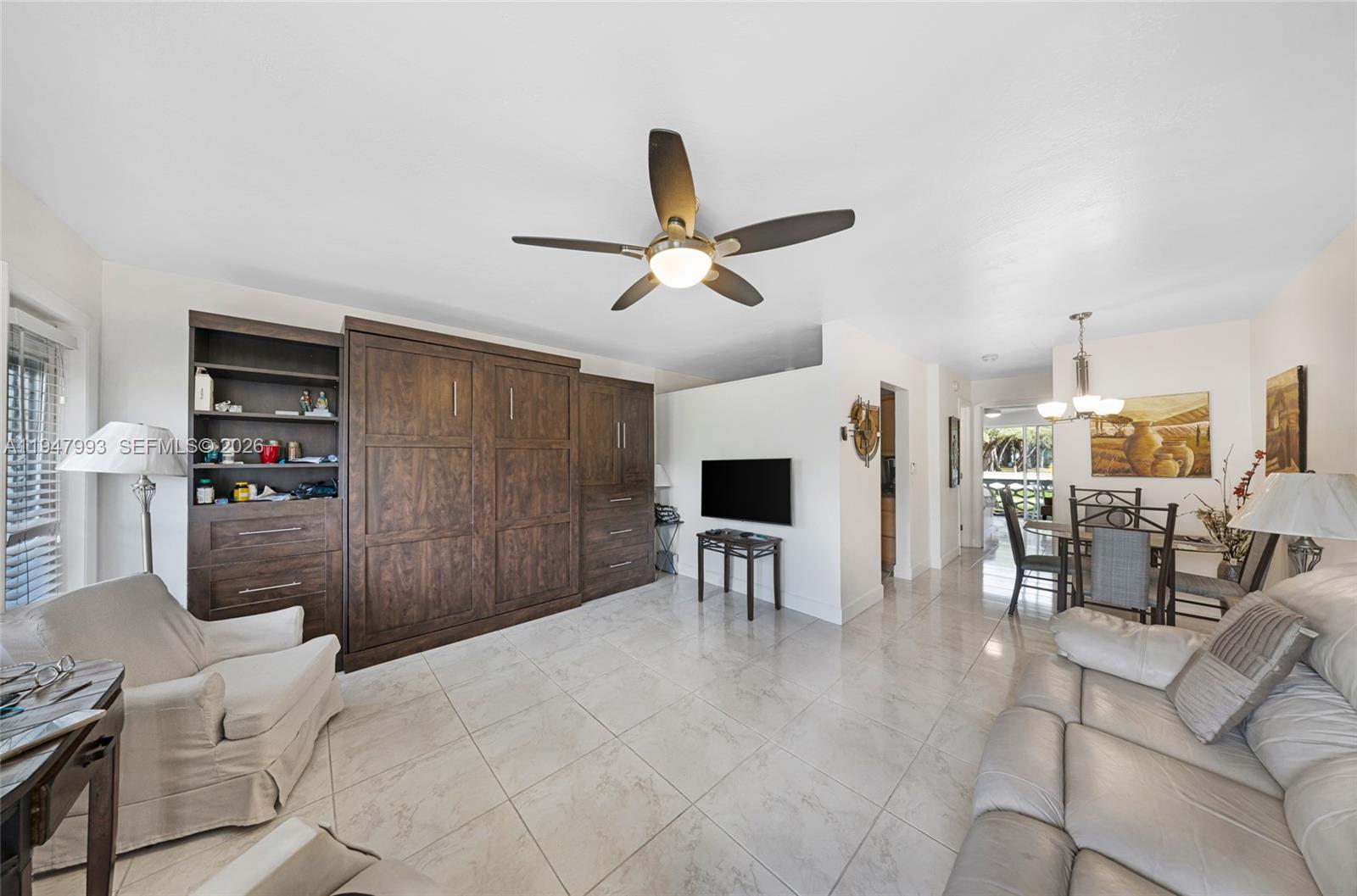 A living room features a large wooden wall unit, tile flooring, and an adjacent dining area — 15610 NE 6th Ave # 9B, Miami FL 33162, MIAMI, FL