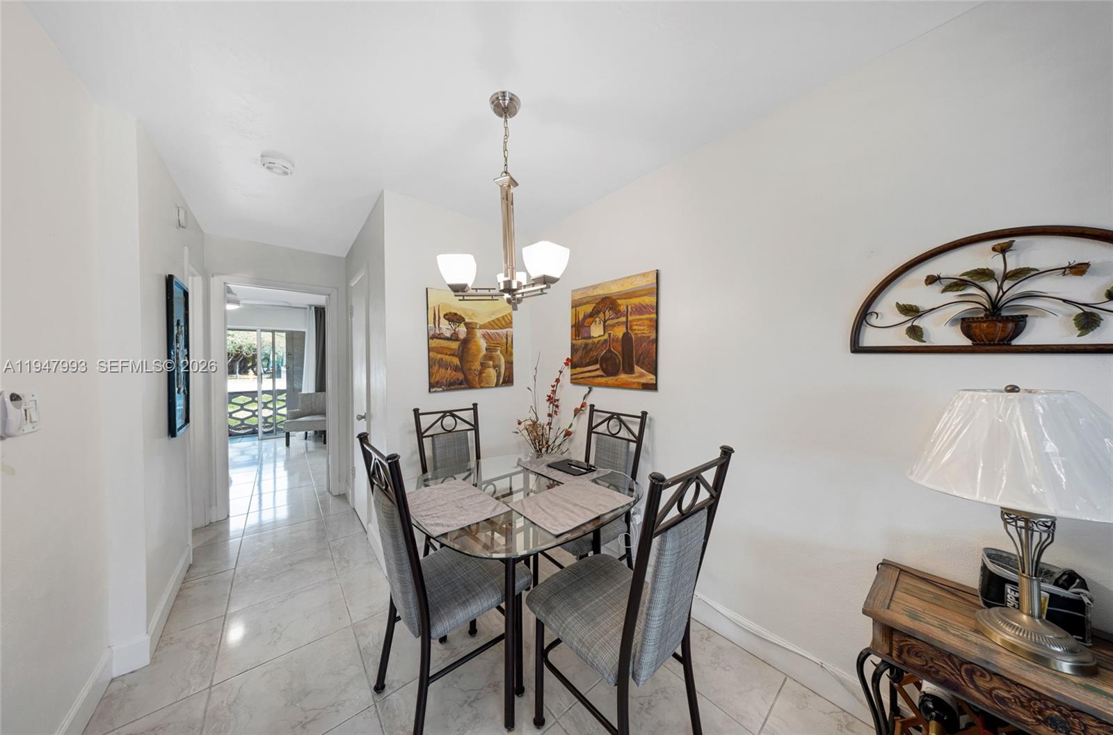 A dining area features a glass-topped table, four chairs, and a chandelier on tiled floors — 15610 NE 6th Ave # 9B, Miami FL 33162, MIAMI, FL