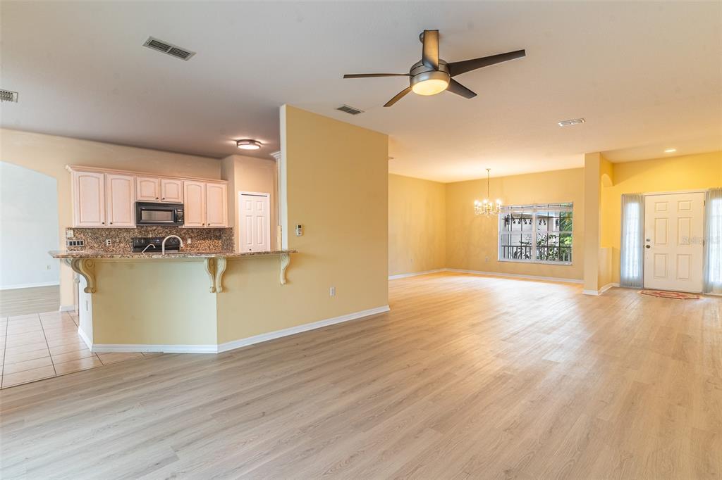 An open-concept living area features light wood flooring, a kitchen with white cabinets, and a foyer — 157 SAND PIPER DRIVE, KISSIMMEE, FL