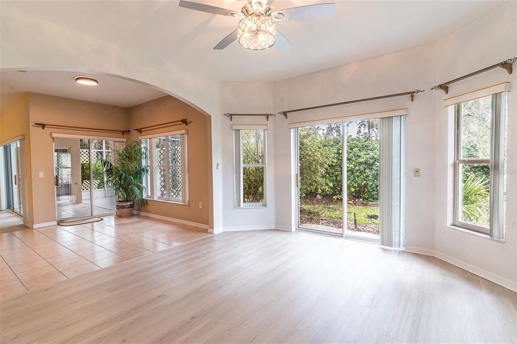 A living room with light wood-look flooring connects to a tiled sunroom through an arched opening — 157 SAND PIPER DRIVE, KISSIMMEE, FL