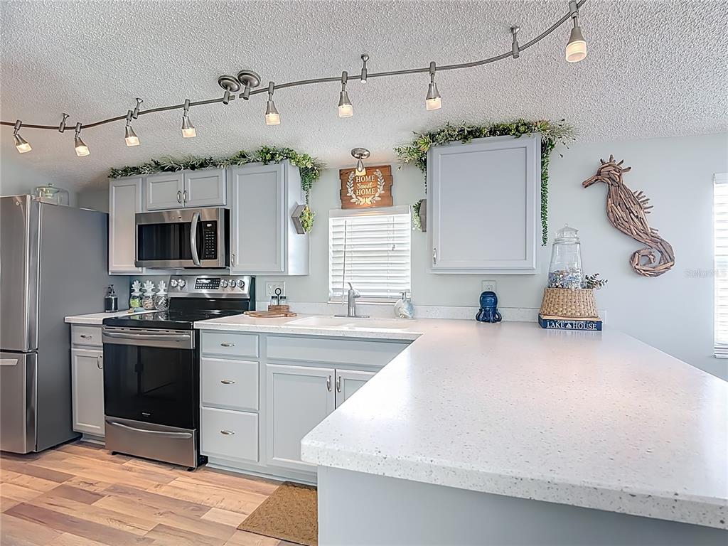 A kitchen features light gray cabinets, white speckled countertops, stainless steel appliances, and track lighting — 9000 US HWY 192 # 537 UNIT 537, CLERMONT, FL