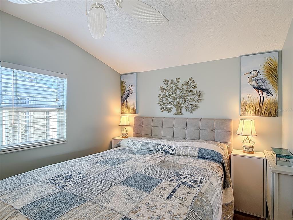 A bedroom features a tufted headboard, patchwork quilt, wall art, and two bedside lamps — 9000 US HWY 192 # 537 UNIT 537, CLERMONT, FL