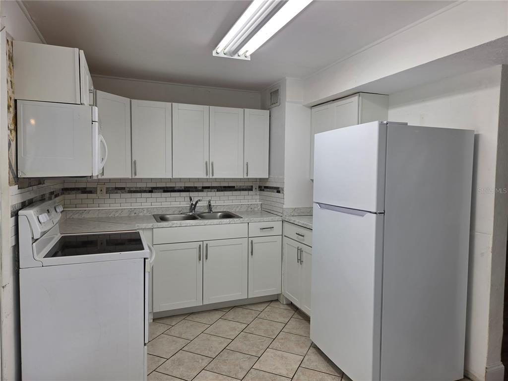 A kitchen features white cabinets, a white refrigerator, a white stove, and tiled flooring — 769 GREENWAY PLACE, DAYTONA BEACH, FL