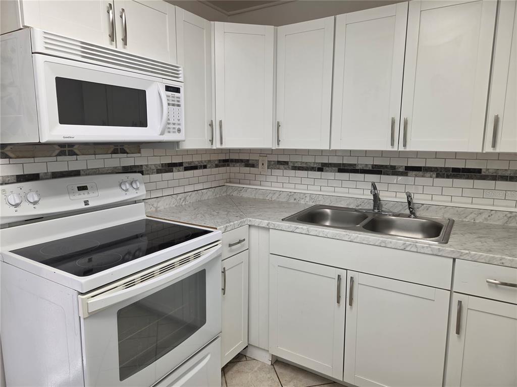 A kitchen features white cabinets, a white stove, a microwave, and a marble-patterned countertop — 769 GREENWAY PLACE, DAYTONA BEACH, FL