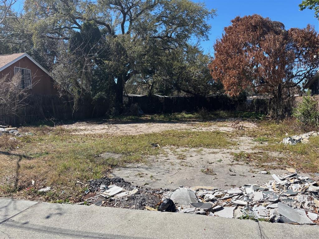 A vacant, debris-strewn residential lot features a concrete slab, patchy grass, and mature trees — 1630 S RIO GRANDE AVENUE, ORLANDO, FL