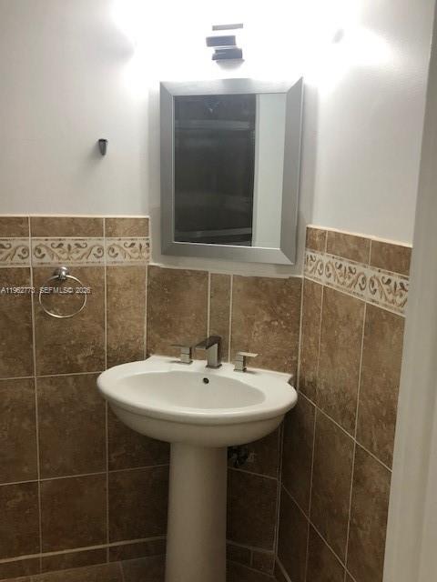 A bathroom features a pedestal sink, a silver-framed mirror, and brown tiled walls — 1201 NE 191st St # G411, Miami FL 33179, MIAMI, FL