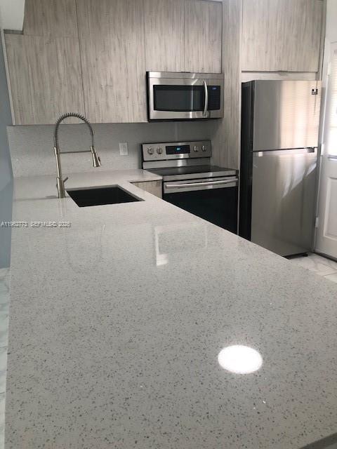 A modern kitchen features light wood cabinets, stainless steel appliances, and a large quartz countertop — 1201 NE 191st St # G411, Miami FL 33179, MIAMI, FL