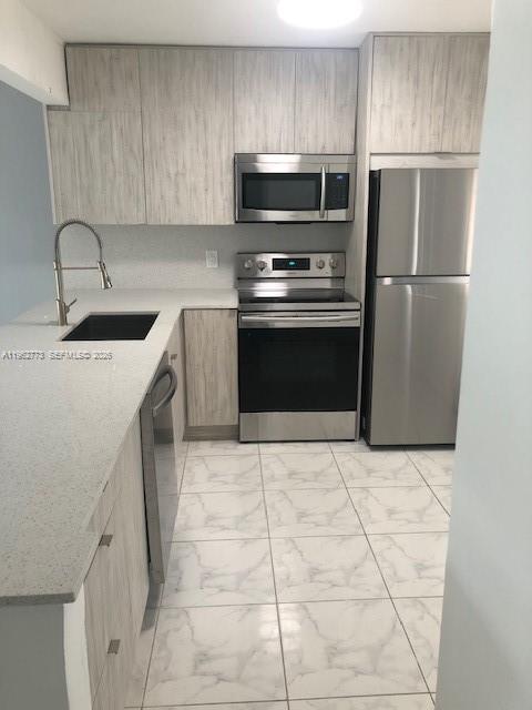 A modern kitchen features light wood cabinets, stainless steel appliances, and white marble-patterned tile flooring — 1201 NE 191st St # G411, Miami FL 33179, MIAMI, FL