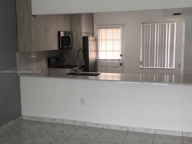A kitchen features white countertops, light wood-toned cabinets, stainless steel appliances, and tiled flooring — 1201 NE 191st St # G411, Miami FL 33179, MIAMI, FL