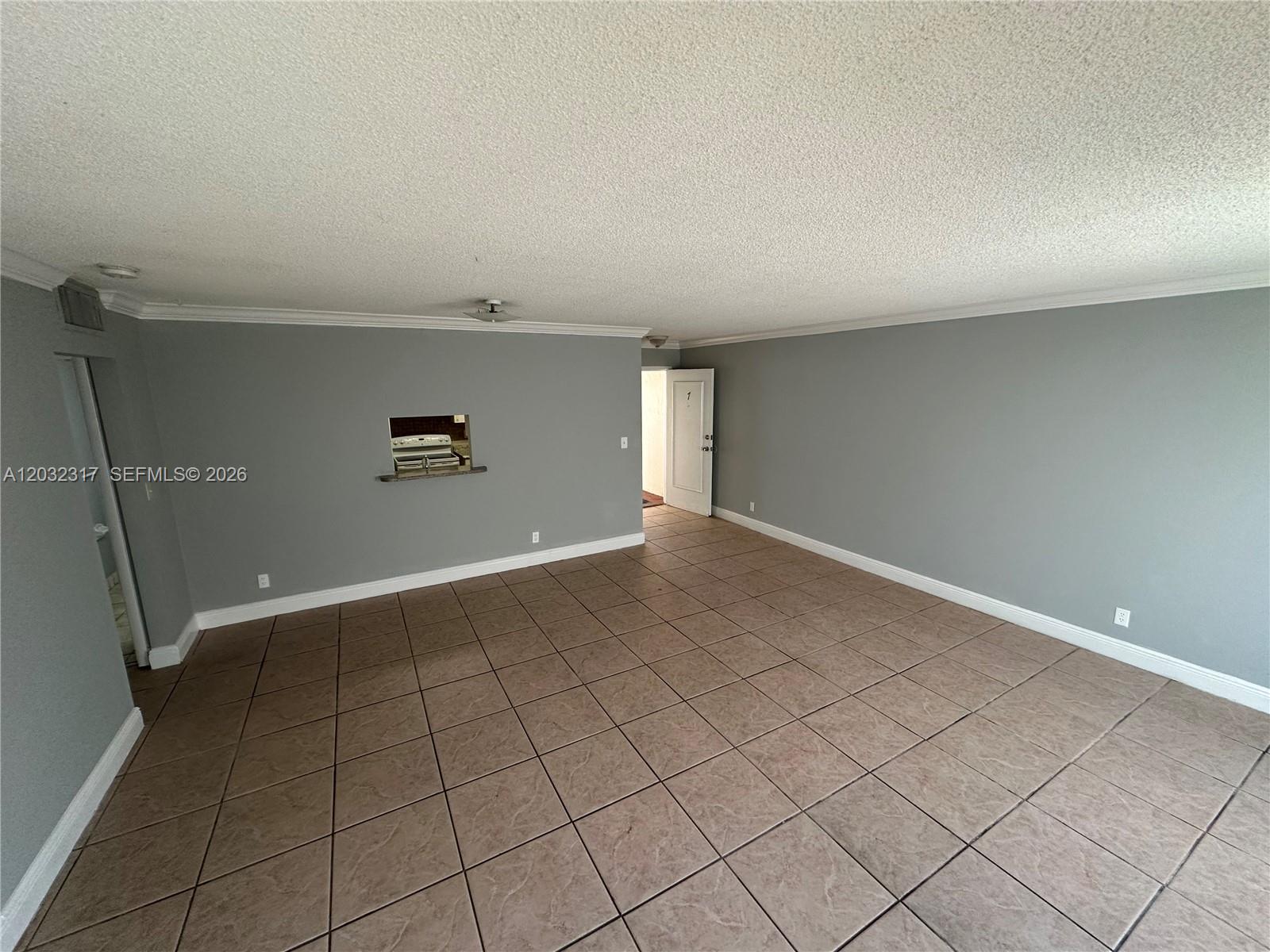 An empty living room features gray walls, brown tile flooring, and a kitchen pass-through window — 2008 JACKSON ST # 7, Hollywood FL 33020, HOLLYWOOD, FL