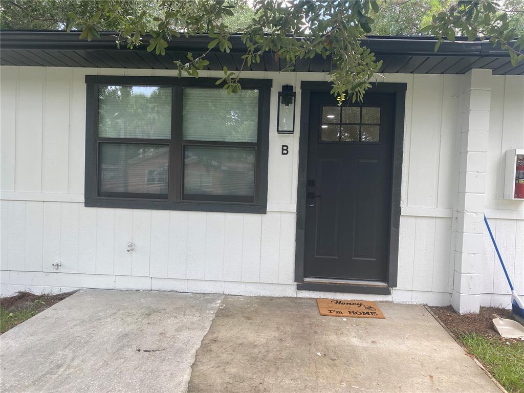 A white exterior wall features a black front door, a window, and a concrete patio — 704 ANGELINA LANE UNIT B, LAKELAND, FL