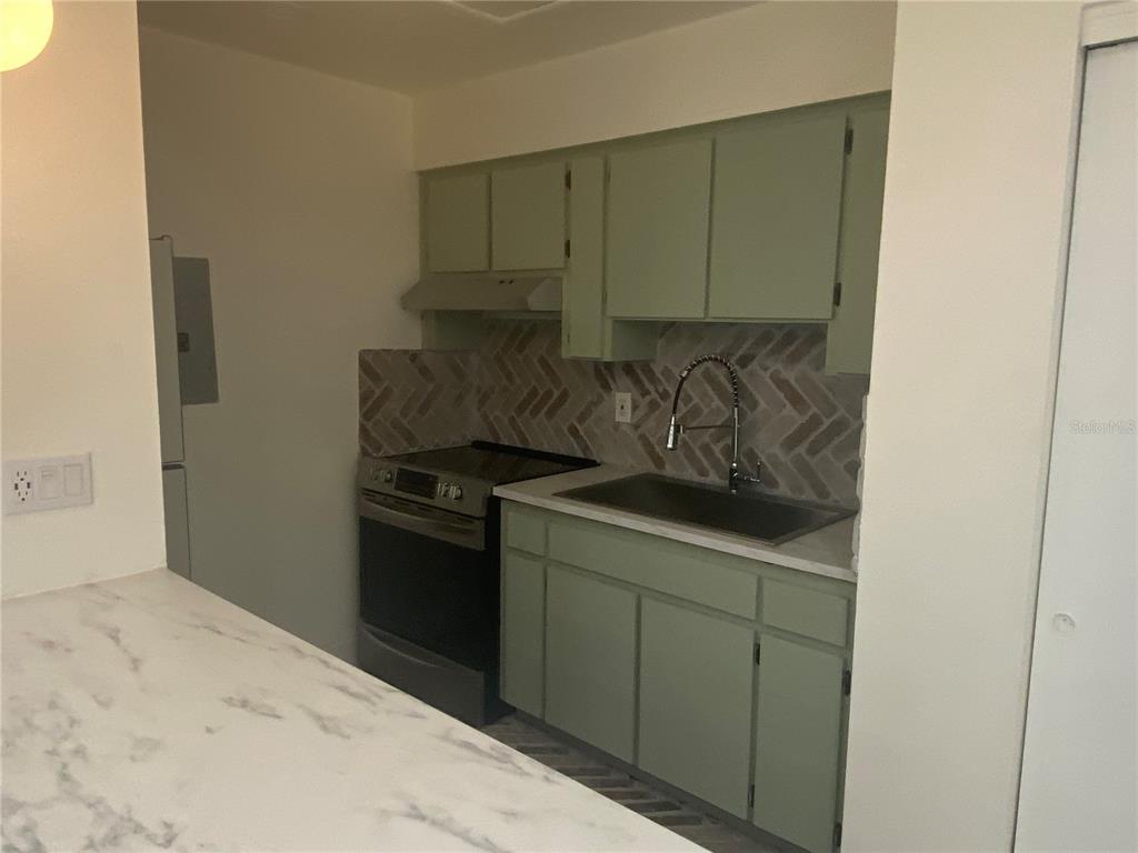 A kitchen features light green cabinets, a herringbone tile backsplash, and a stainless steel stove — 704 ANGELINA LANE UNIT B, LAKELAND, FL
