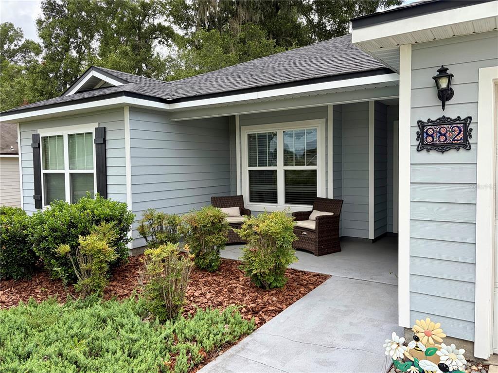 A light blue house exterior features a covered porch with two chairs and landscaping — 882 NW 256TH WAY, NEWBERRY, FL