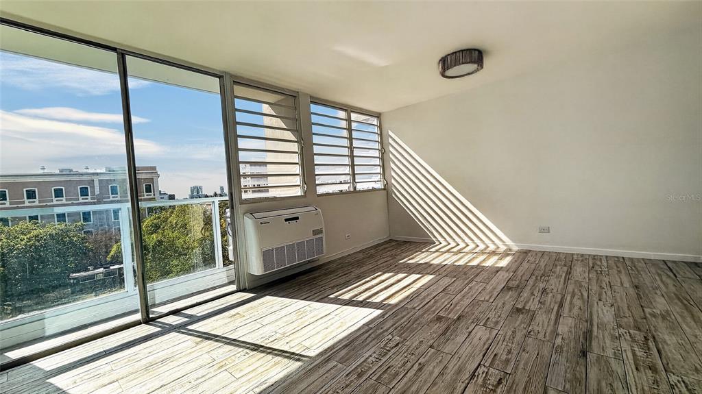 A sunlit room features wood-look tile flooring, a wall-mounted air conditioner, and large sliding glass doors — 501 ELISA COLBERG, MIRAMAR Apt 4-E, SAN JUAN, PR