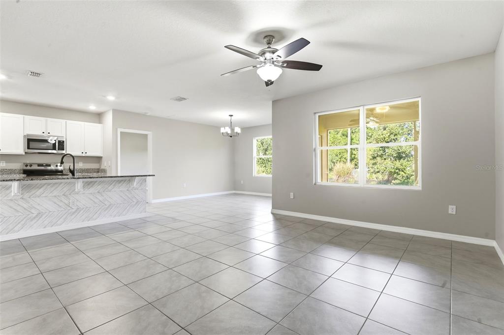 A bright, open-concept living area features light gray tile flooring, white kitchen cabinets, and a ceiling fan — 895 LAZIO CIRCLE, DEBARY, FL