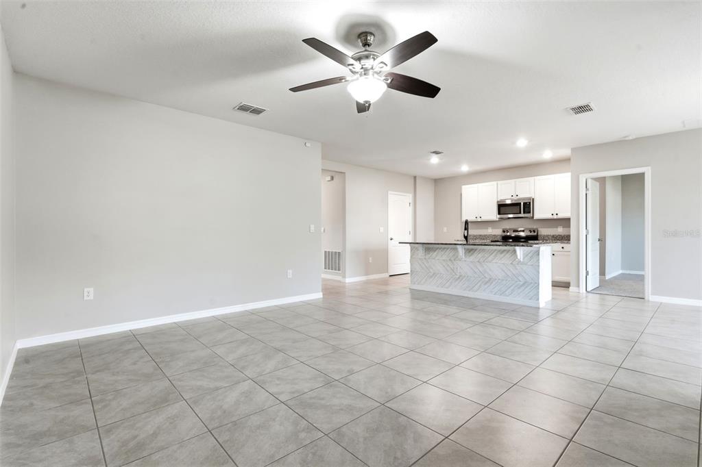 An open-concept living area features gray tile flooring, a ceiling fan, and a kitchen island — 895 LAZIO CIRCLE, DEBARY, FL