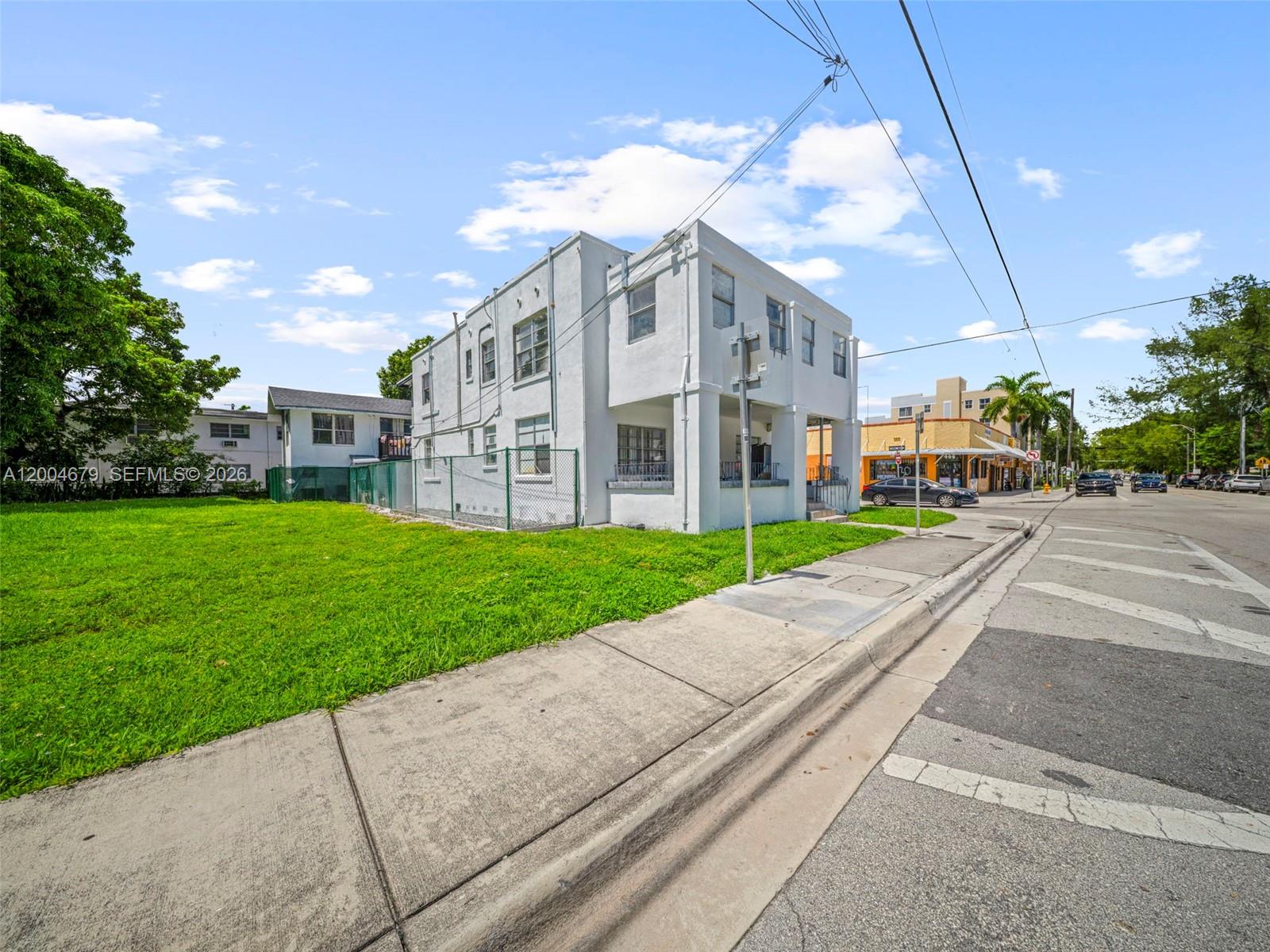 A two-story white building stands next to a large grassy lot along a street — 500 SW 8th AVE, Miami FL 33130, MIAMI, FL