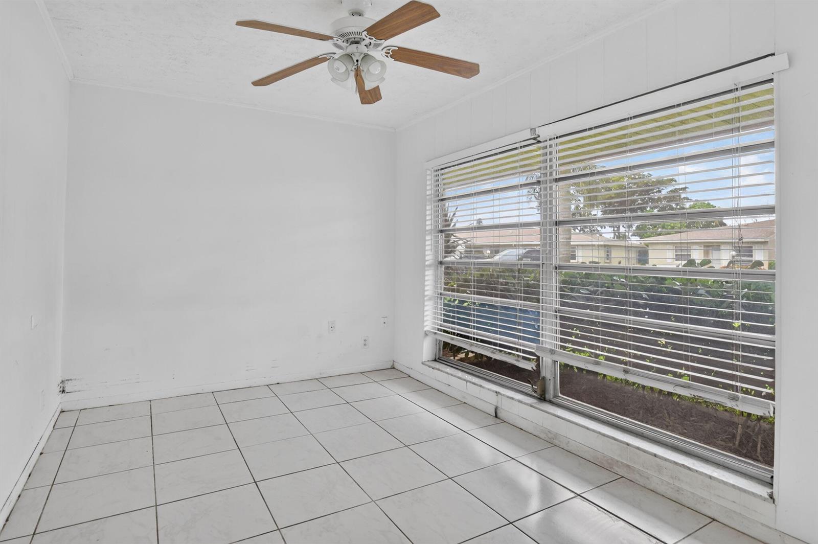 An empty room features white tiled floors, plain white walls, and a large window with blinds — 20923 Sedgewick Drive # 386, Boca Raton FL 33433, BOCA RATON, FL
