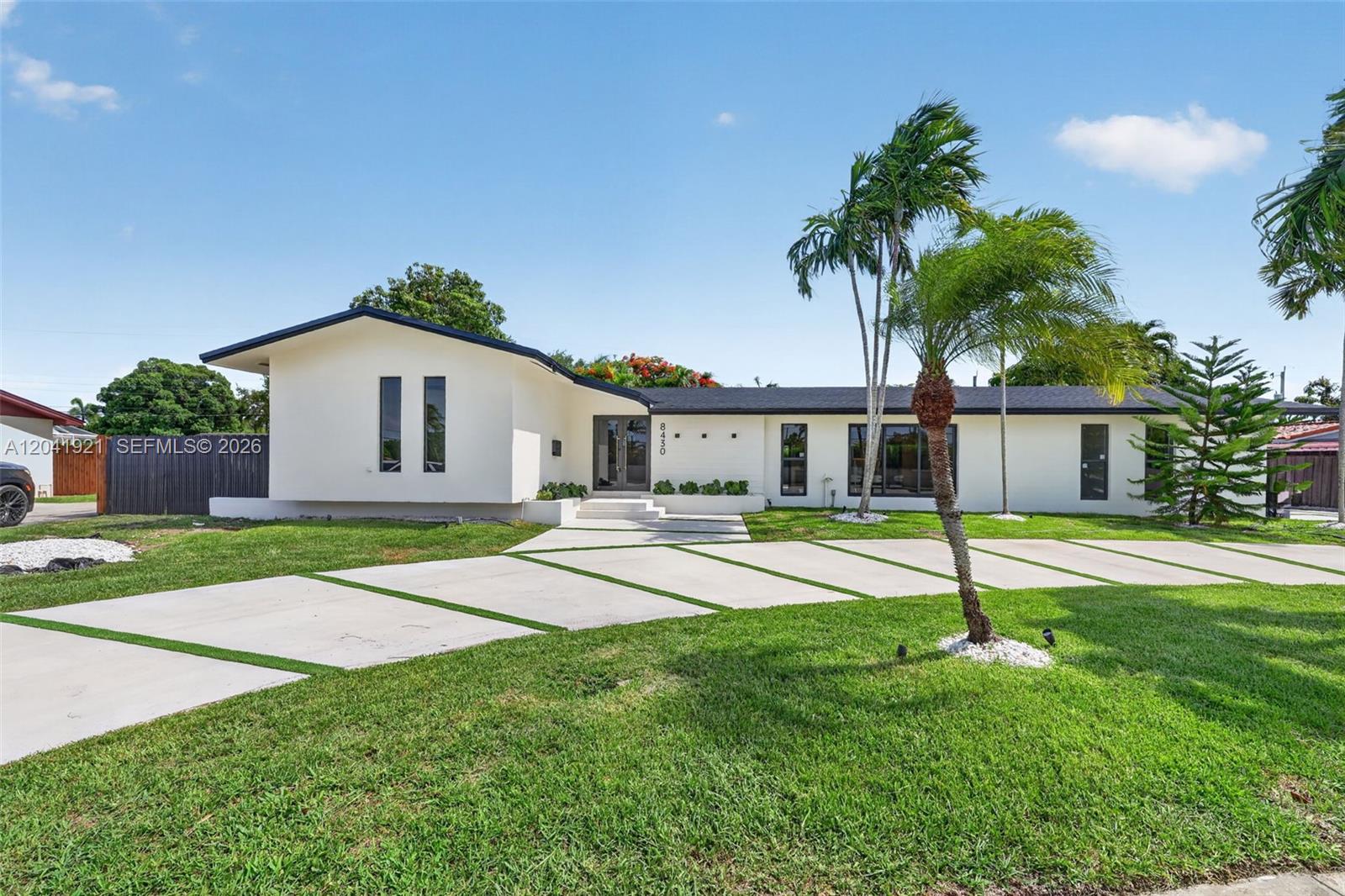 A single-story white house with a modern driveway and palm trees sits on a lawn — 8430 SW 88th St, Miami FL 33156, MIAMI, FL