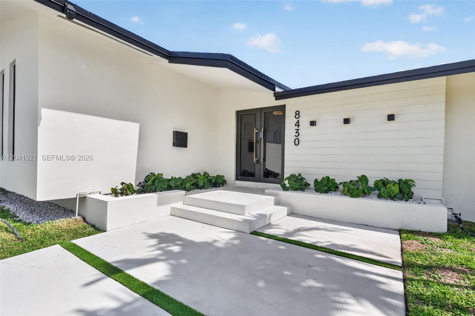 The exterior of a modern home features a white facade, double glass doors, and planters — 8430 SW 88th St, Miami FL 33156, MIAMI, FL