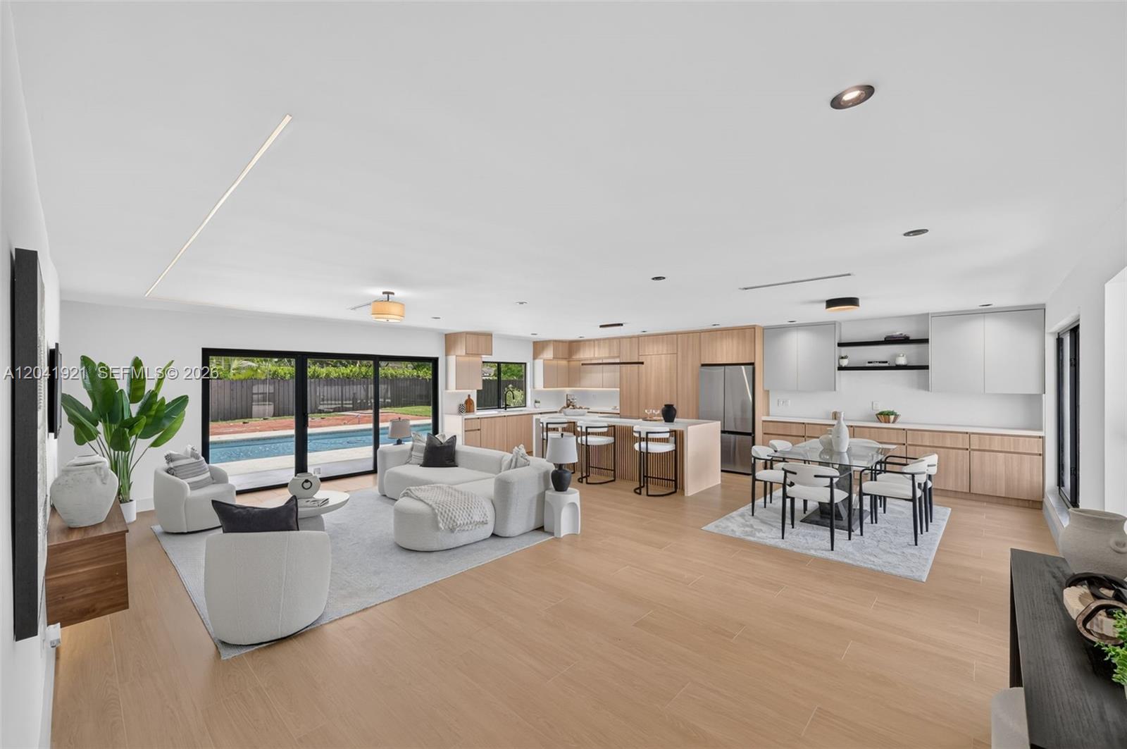 An open-concept living, dining, and kitchen area features light wood flooring and a backyard pool — 8430 SW 88th St, Miami FL 33156, MIAMI, FL