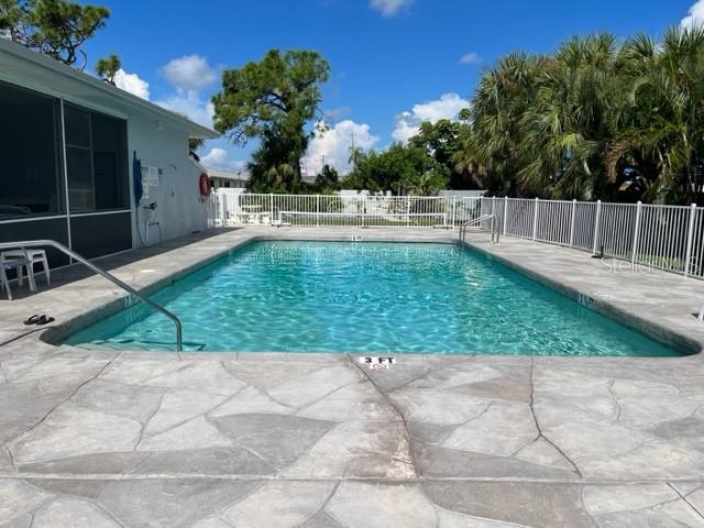 A rectangular swimming pool with a stone deck sits beside a house with a screened porch — 6527 HAMLET DRIVE UNIT 26-A, ENGLEWOOD, FL