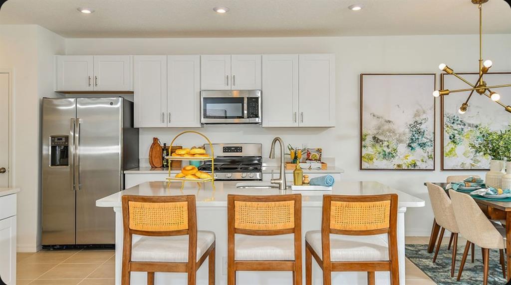 A modern kitchen features white cabinets, a large quartz island, and stainless steel appliances — 13832 SHELLMORE AVENUE, PALMETTO, FL