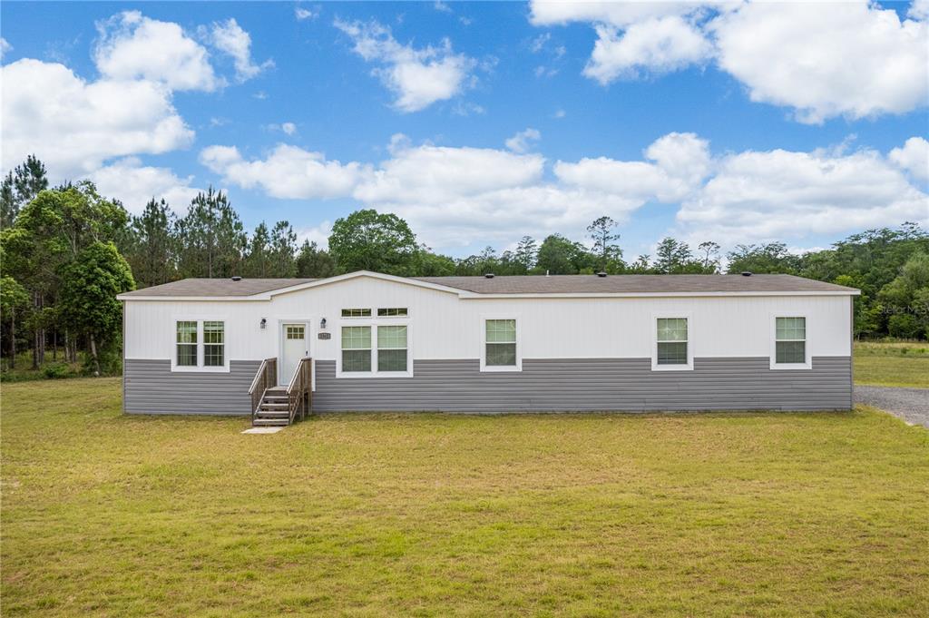 A single-story manufactured home with white and gray horizontal siding sits on a grassy lot — 2362 NE COUNTY ROAD 1469, HAWTHORNE, FL