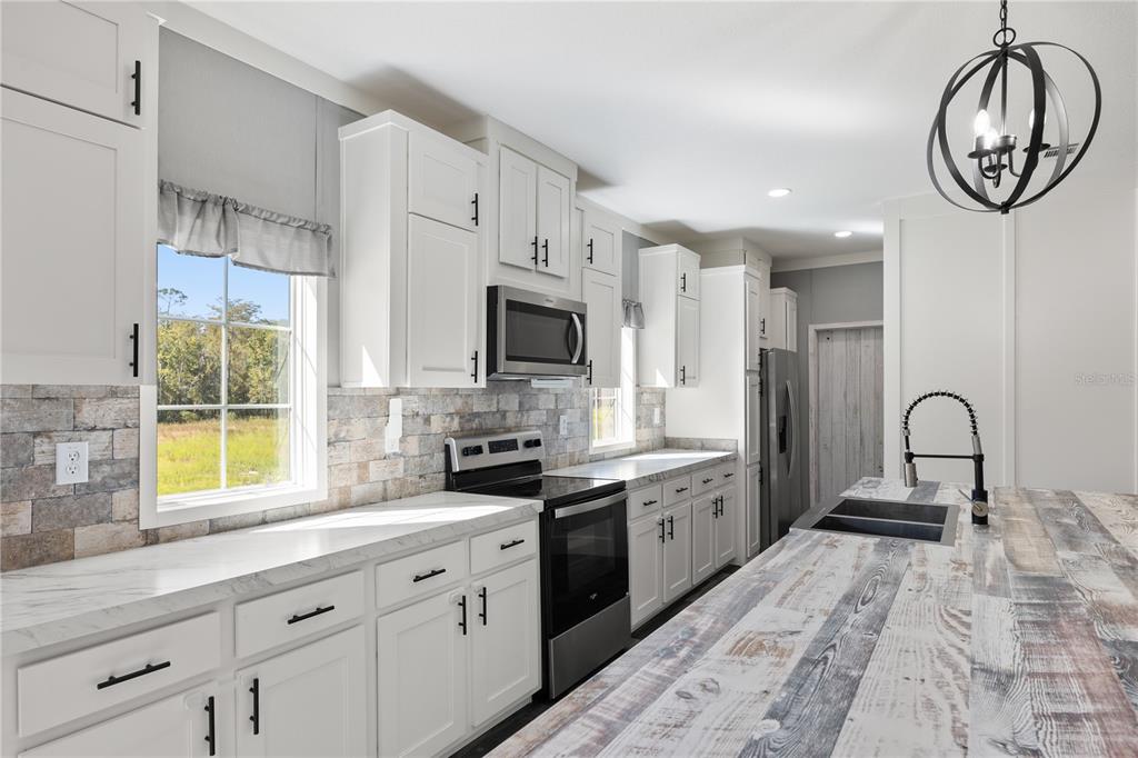 A kitchen features white cabinets, stainless steel appliances, a stone backsplash, and a wood-look island — 2362 NE COUNTY ROAD 1469, HAWTHORNE, FL