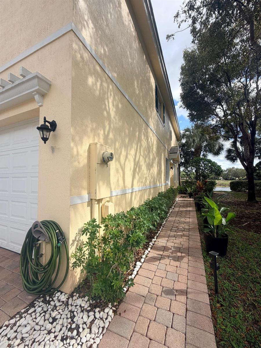 A paved walkway runs alongside the yellow stucco exterior wall of a house — 7644 Foxcroft Lane # 7644, Davie FL 33328, DAVIE, FL