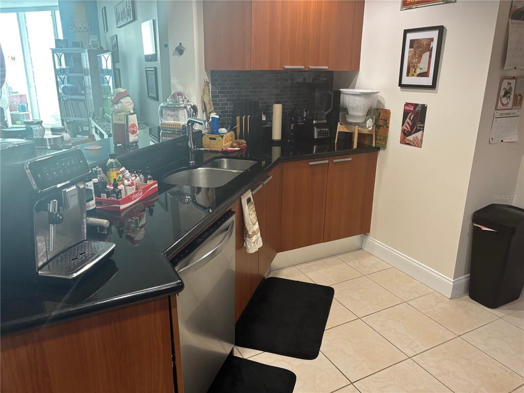 A kitchen features wood cabinets, black countertops, stainless steel appliances, and a tiled floor — 241 RIVERSIDE DRIVE UNIT 2308, HOLLY HILL, FL