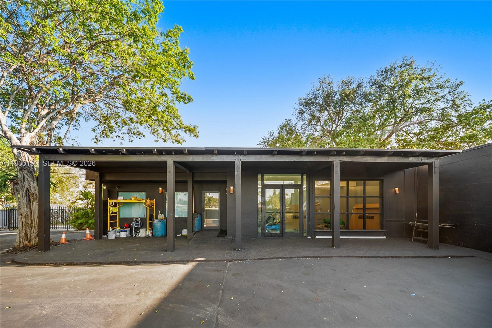 The exterior of a dark-painted commercial building features a covered patio and large glass doors — 100 NW 36th St, Miami FL 33127, MIAMI, FL